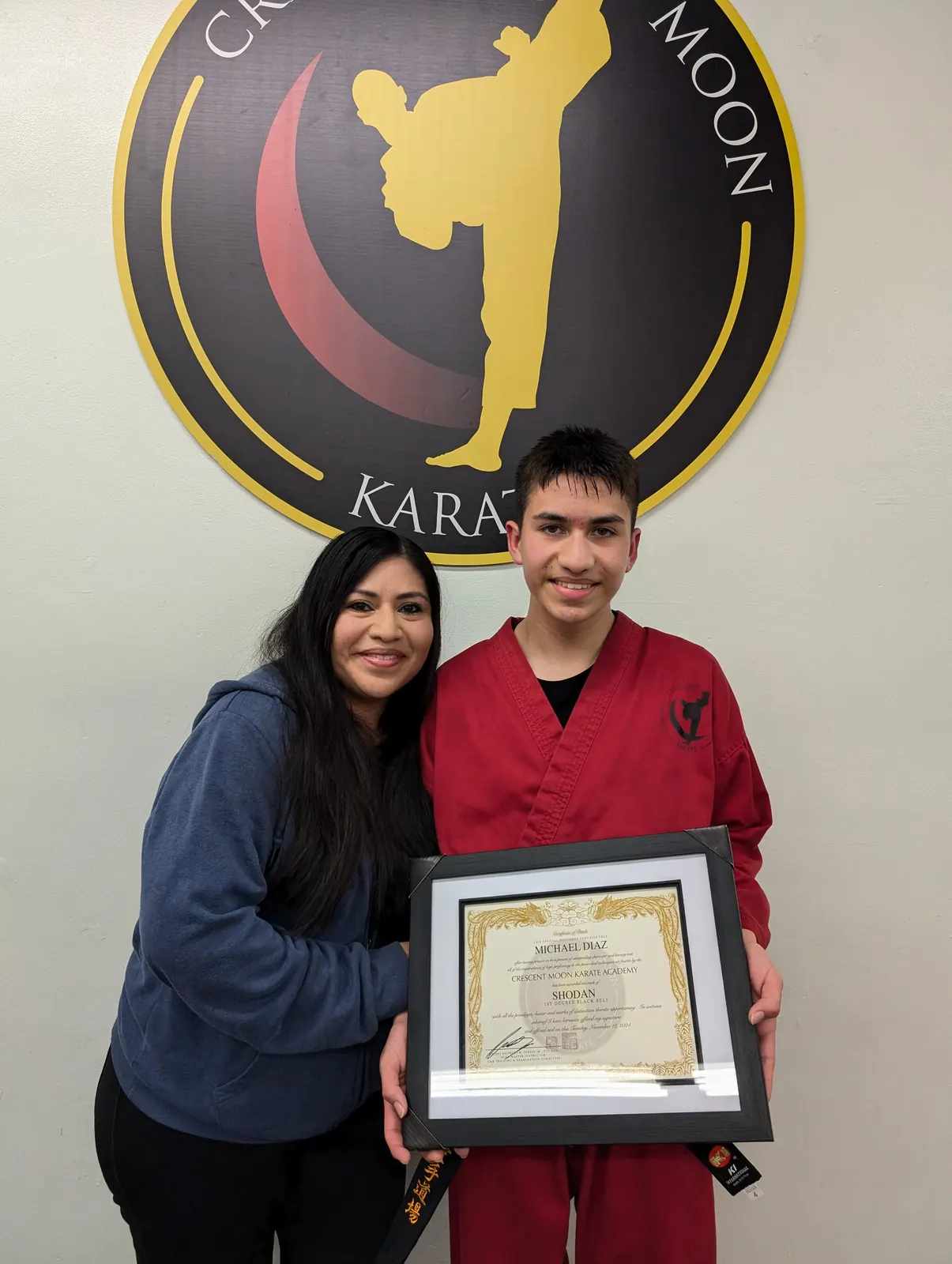 A student in a red gi standing with a family member inside the dojo